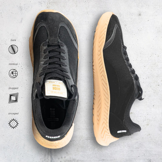Black barefoot and minimal sneakers with tan soles on a gray surface