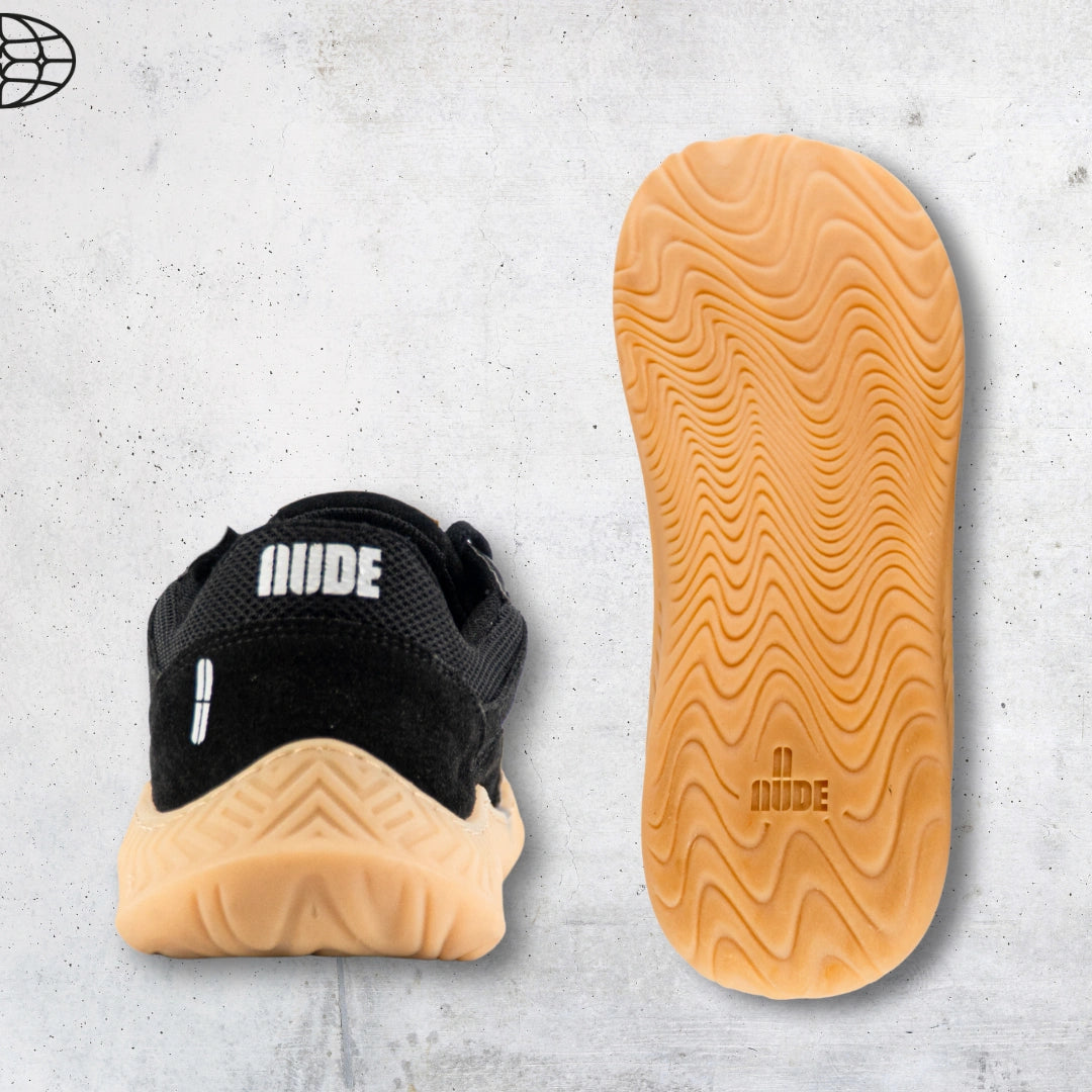 Black barefoot and minimal sneaker with tan sole and 'NUDE' branding on a gray concrete surface