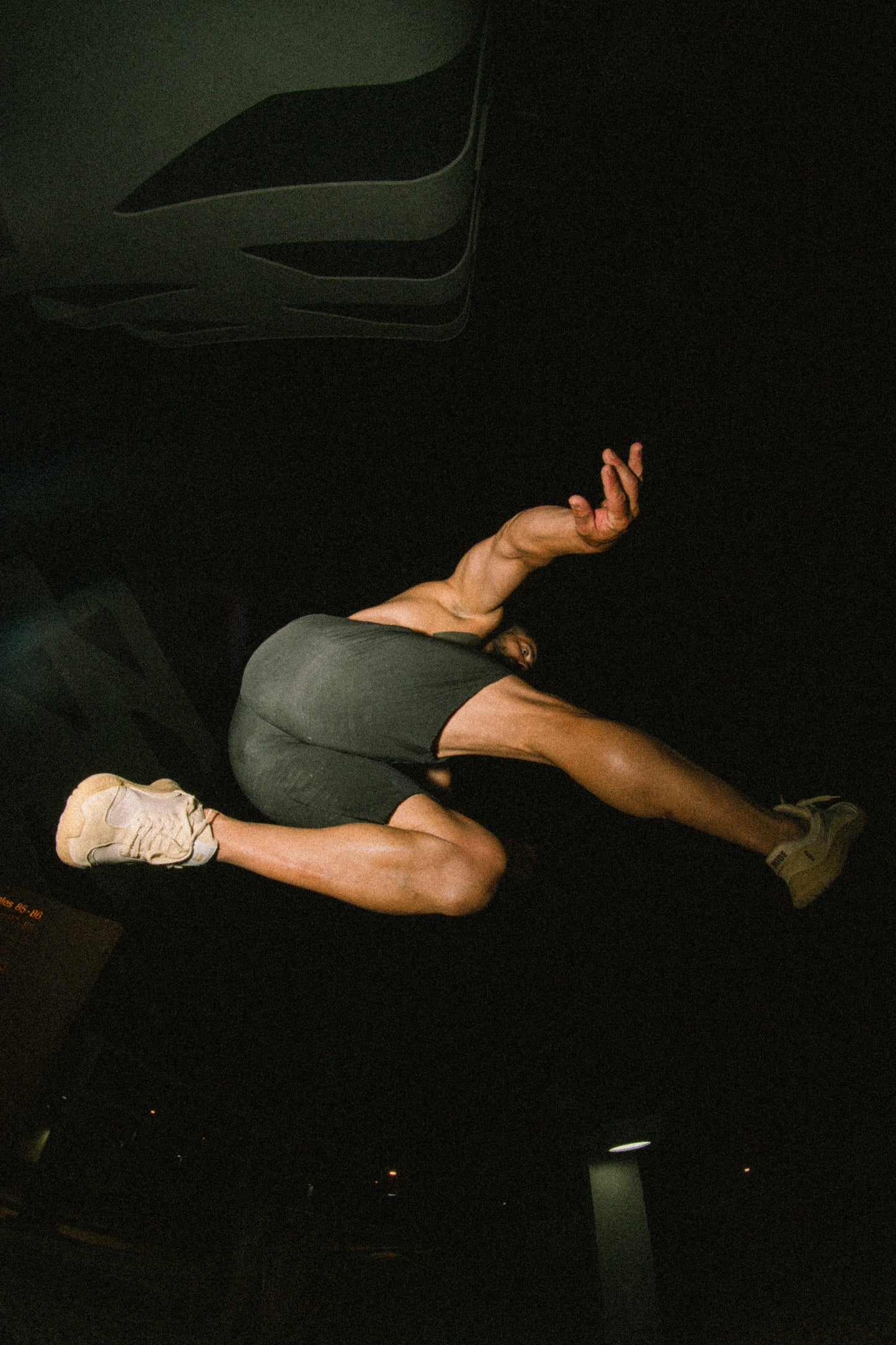 Person in athletic wear performing a split on a dark background with barefoot and minimal sneakers