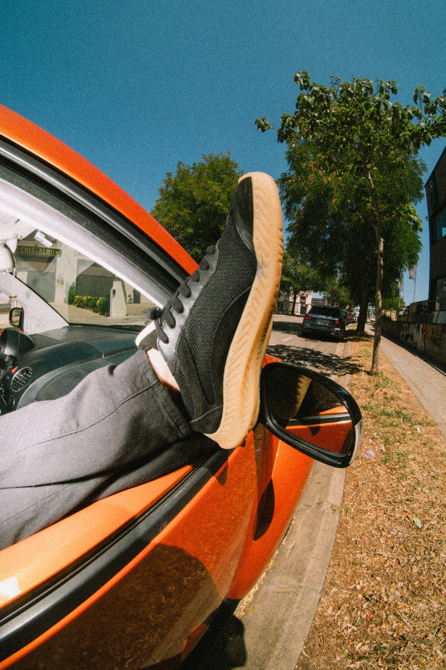 Person's foot with a black barefoot and minimal shoe stepping out of an open car door on a sunny day.