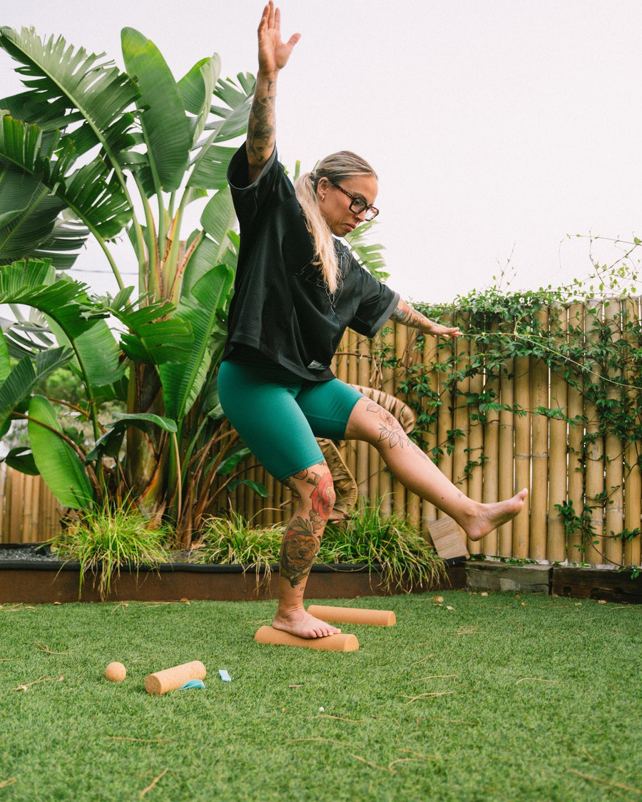 Woman doing a barefoot balance exercise on The Nude Foot cork rollers as part of a foot mobility routine
