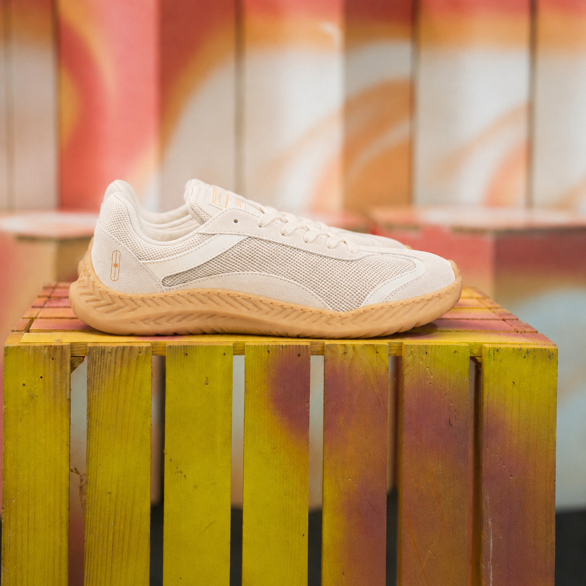 The Nude Foot Barefoot Sneaker Aura - single off-white and beige sneaker with tan sole on a yellow wooden crate