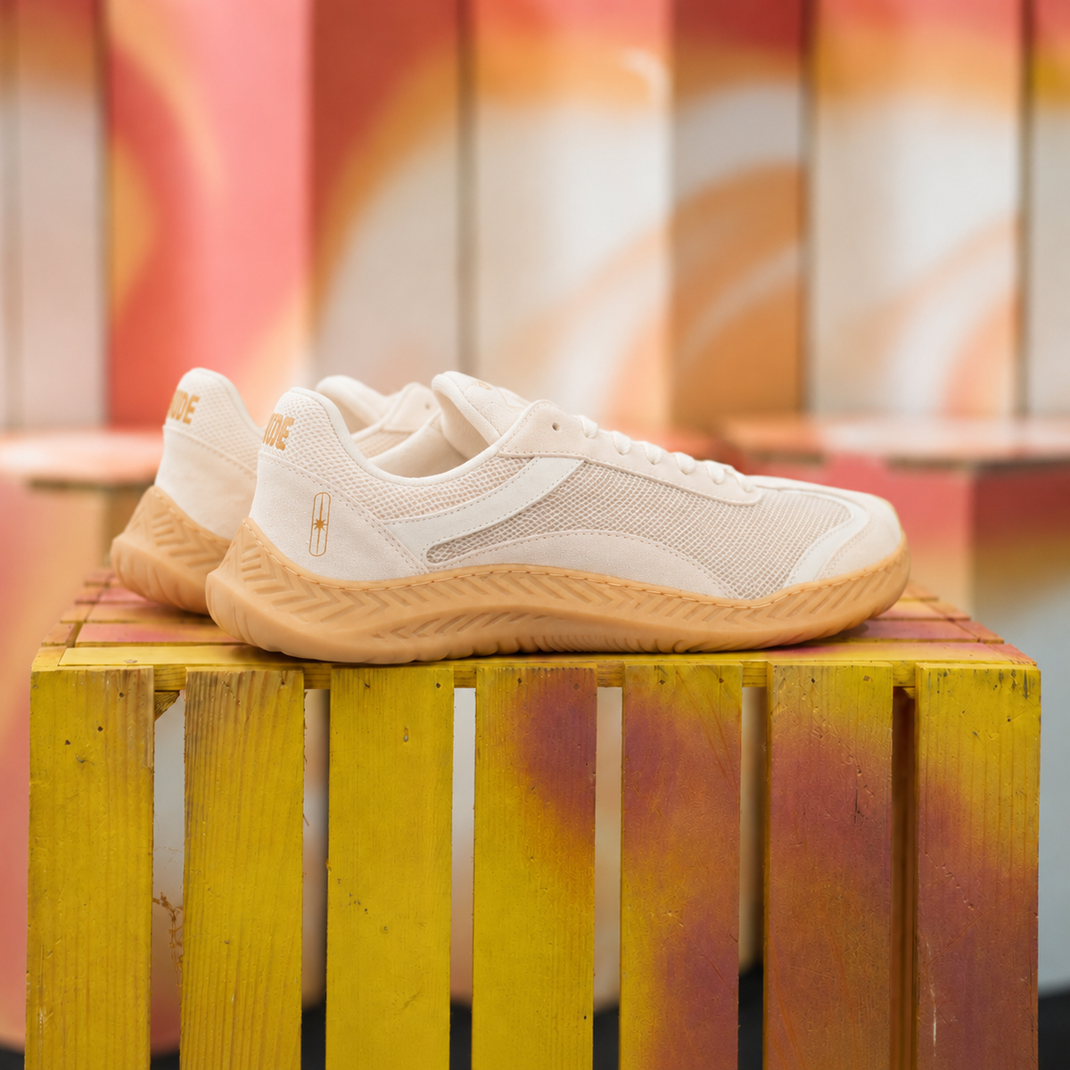 The Nude Foot Barefoot Sneaker Aura - pair of off-white mesh sneakers with gum sole, angled side view on wooden crate