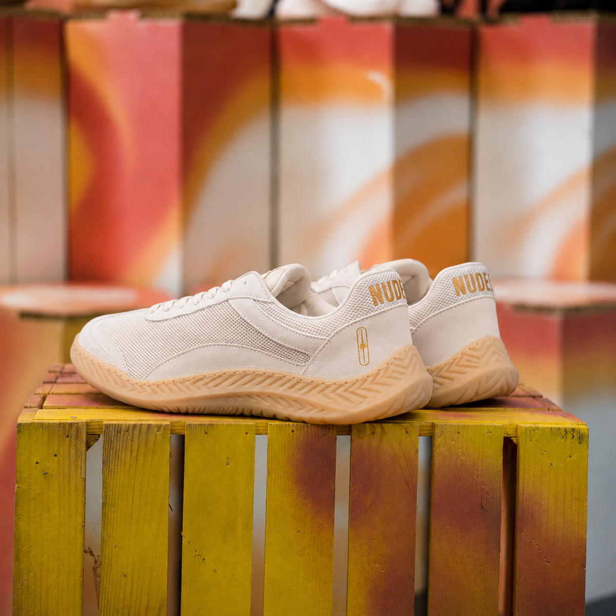 The Nude Foot Barefoot Sneaker Aura - off-white sneakers with gold NUDE branding, side profile on wooden crate