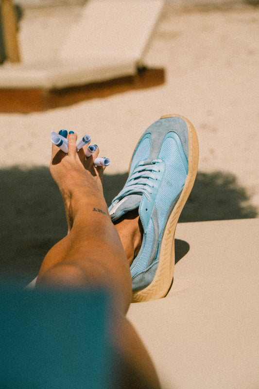 Person wearing blue sneakers with beige soles on a sandy surface