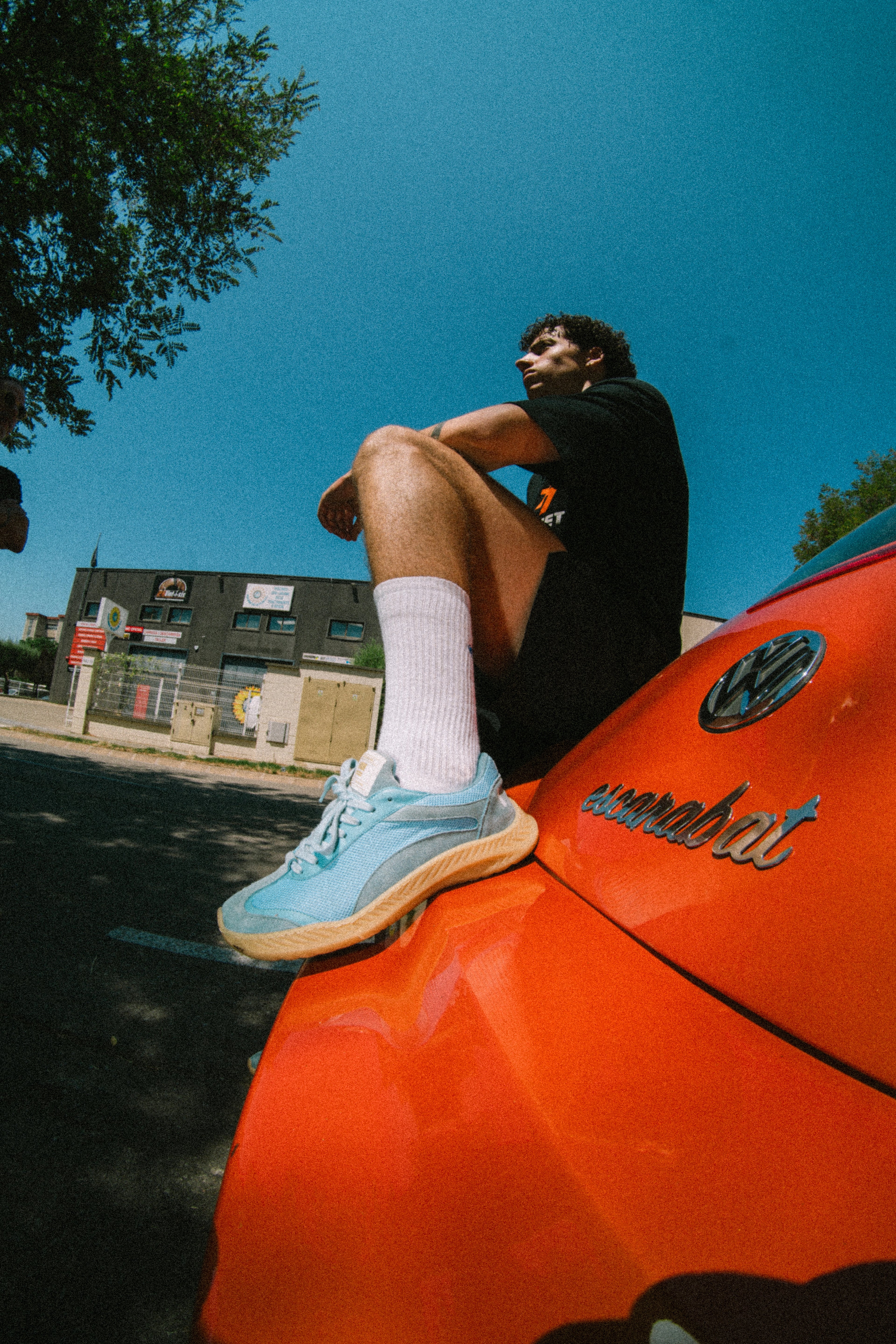 Person sitting on a red Volkswagen Beetle with barefoot and minimal  snakers